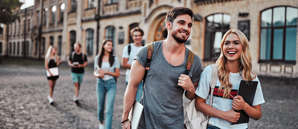 Eine Gruppe von Studenten schlendert entspannt die Straße entlang und lacht miteinander.