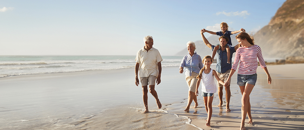 Eine Familie spaziert am Strand, umarmt sich und genießt die gemeinsame Zeit in der Sonne.