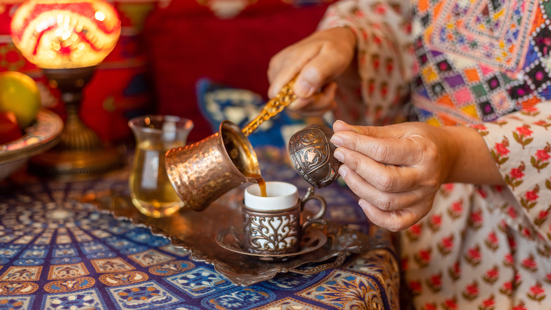 Auf orientalisch gemusterter Tisch wird türkischer Tee wird in verzierte Tasse gekippt.