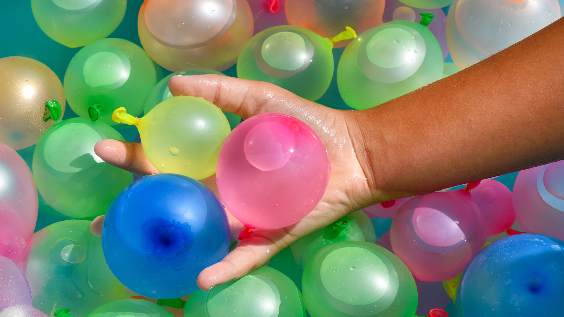 Viele bunte Wasserbomben und eine Hand greift nach drei Wasserbomben.