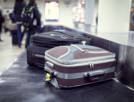 Das Bild zeigt zwei Gepäckstücke auf einem Gepäckband in einem Flughafen, was auf Reisen und möglicherweise auf den Abschied oder die Ankunft von Reisenden hindeutet.